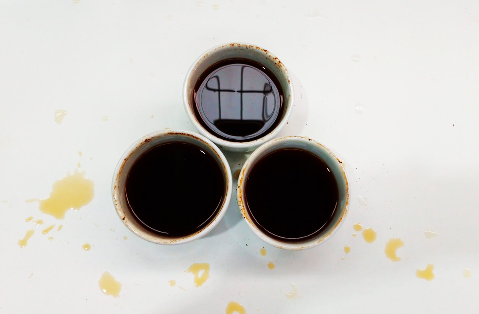 Aerial shot of three cups of black coffee on white table with coffee spills